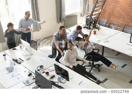 Happy employees enjoy funny competition riding on chairs in offi 65012749
