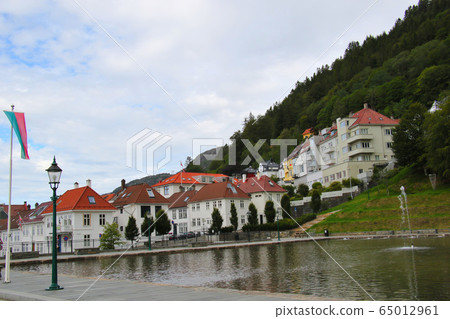 Pond with fountain and houses on the hillside of Mt. Floyen mountain trail in Bryggen, the world heritage of Bergen Pond with fountain and houses on the hillside of Mt. Floyen mountain trail in Bryggen, the world heritage of Bergen 65012961