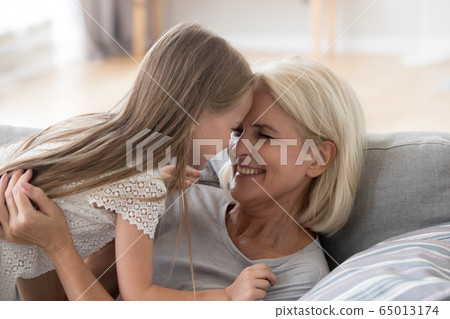 Cute granddaughter having fun playing with grandmother embracing 65013174