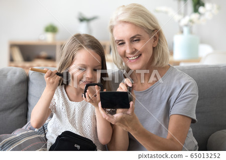 Happy granddaughter applying blush having fun doing makeup with 65013252