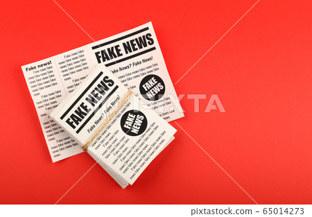 Stack of FAKE NEWS newspapers over red 65014273
