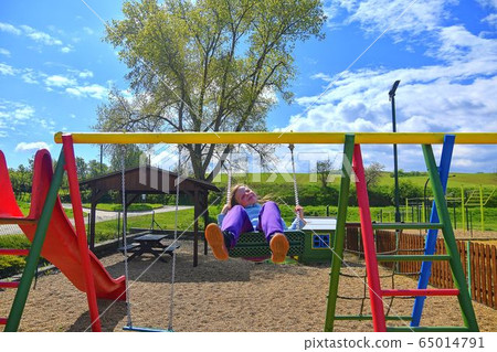 Child playing on outdoor playground. Kid play on school or kindergarten yard. Active kid on colorful swing. Healthy summer activity for children in sunny weather. 65014791