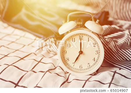 White vintage alarm clock and pillows in the bed. White vintage alarm clock and pillows in the bed. 65014907