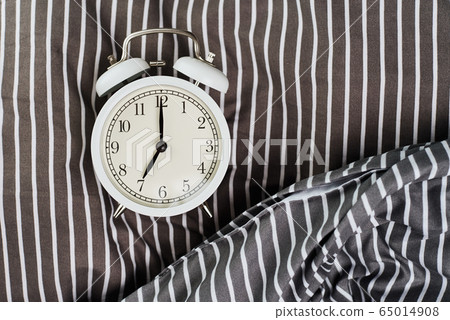 White vintage alarm clock on pillow in the bed. White vintage alarm clock on pillow in the bed. 65014908