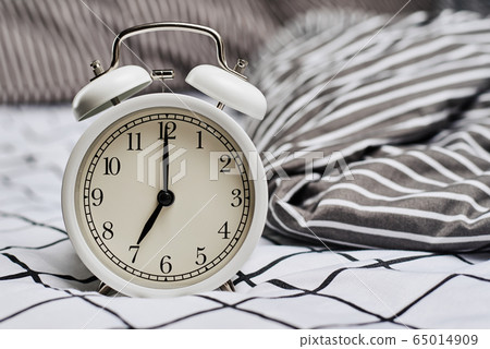 White vintage alarm clock and pillows in the bed. White vintage alarm clock and pillows in the bed. 65014909