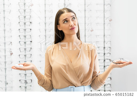 Pensive woman choosing between eyeglasses and contacts 65015182