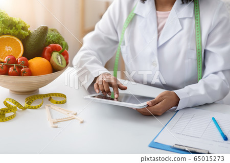 Black woman dietician working with digital tablet at clinic 65015273
