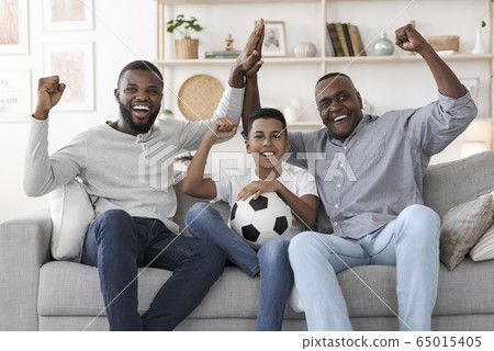 Excited African Dad, Son And Grandfather Watching Football On Tv And Cheering 65015405