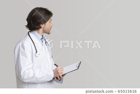 Confident doctor writing notes on clipboard and looking at copy space Confident doctor writing notes on clipboard and looking at copy space 65015616