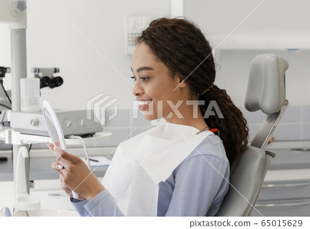 Beautiful black lady checking her white smile in mirror Beautiful black lady checking her white smile in mirror 65015629