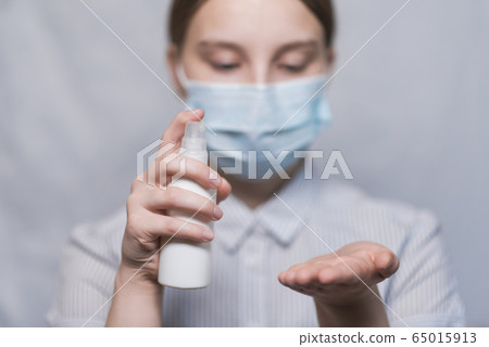 teenager girl of 12-15 years old, medical mask covers face, holds antiseptic spray in hand, disinfects hands from viruses bacteria, COVID-19 epidemic pandemic virus outbreak protection concept. teenager girl of 12-15 years old, medical mask covers face, holds antiseptic spray in hand, disinfects hands from viruses bacteria, COVID-19 epidemic pandemic virus outbreak protection concept. 65015913