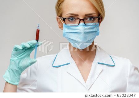 Doctor or woman nurse wearing protective mask holding syringe Doctor or woman nurse wearing protective mask holding syringe 65028347