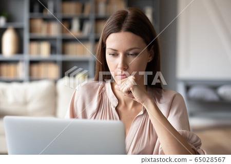 Thoughtful woman looking at laptop screen, pondering project Thoughtful woman looking at laptop screen, pondering project 65028567