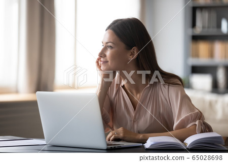 Dreamy young woman pondering ideas, sitting at desk with laptop 65028698