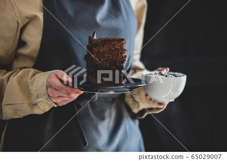 woman in an apron holds cappuccino and chocolate 65029007