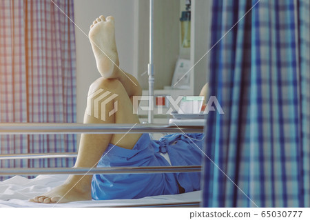 Elderly male patient relaxing on bed with his legs crossed in a good mood to wait for the time to go home. Selective focus on foot sole. Elderly male patient relaxing on bed with his legs crossed in a good mood to wait for the time to go home. Selective focus on foot sole. 65030777