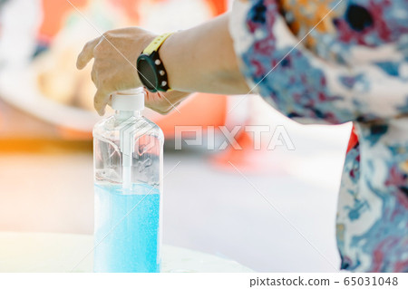 Woman uses her hand to press hand sanitizer bottle to clean her hand at wayside in the city. Concepts of Flu virus, Covid-19 (Coronavirus disease). Selective focus on alcohol gel bottle. 65031048