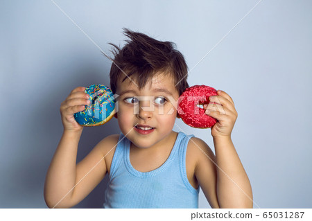 boy is holding two colored doughnuts blue and red in front boy is holding two colored doughnuts blue and red in front 65031287
