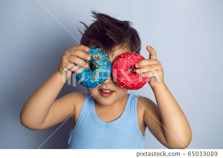 boy is holding two colored doughnuts blue and red in front boy is holding two colored doughnuts blue and red in front 65033089