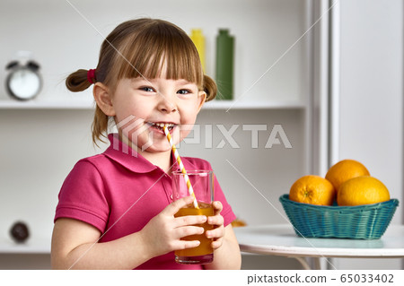 Cute little girl drinks orange juice at home 65033402
