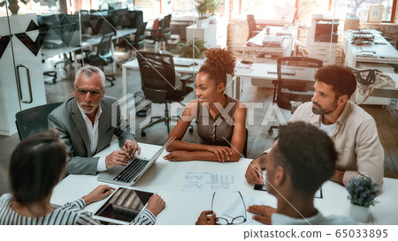 Business meeting. Mature man in formal wear discussing something with coworkers while sitting together at the office table Business meeting. Mature man in formal wear discussing something with coworkers while sitting together at the office table 65033895