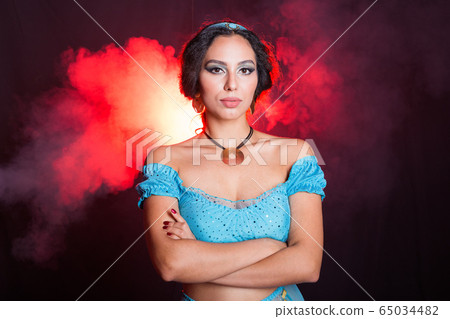 Magic, cosplay, carnival and fairy tale concept - Portrait of a young woman in the image of an Eastern fairy Princess on dark background. Magic, cosplay, carnival and fairy tale concept - Portrait of a young woman in the image of an Eastern fairy Princess on dark background. 65034482