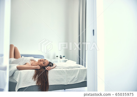 Caucasian girl laying on soft light bed in cozy bedroom 65035975