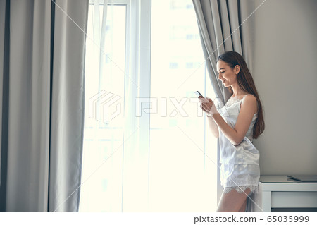 Cute slim girl standing near window and using Internet 65035999
