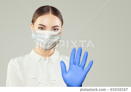 Friendly woman nurse in face mask showing stop Friendly woman nurse in face mask showing stop 65038587