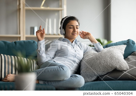 Happy indian girl resting on cozy sofa, listening to music. Happy indian girl resting on cozy sofa, listening to music. 65040304