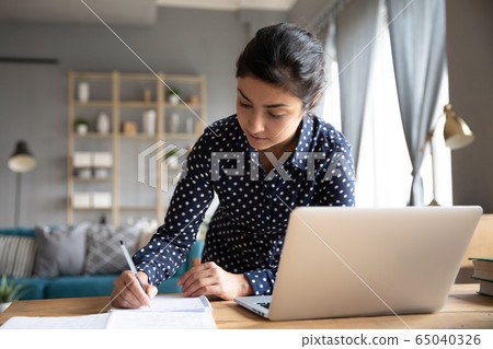 Focused young indian student writing notes from online seminar. Focused young indian student writing notes from online seminar. 65040326