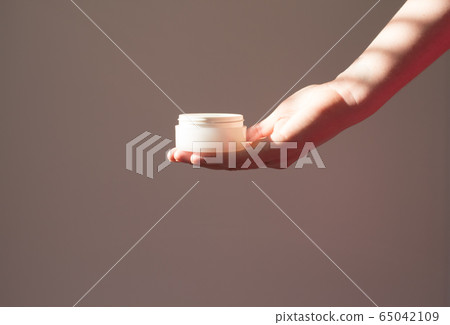 Skin care packaging in female hand.Beauty product for face skin,plant shadow white background. Scincare cosmetic concept Skin care packaging in female hand.Beauty product for face skin,plant shadow white background. Scincare cosmetic concept 65042109