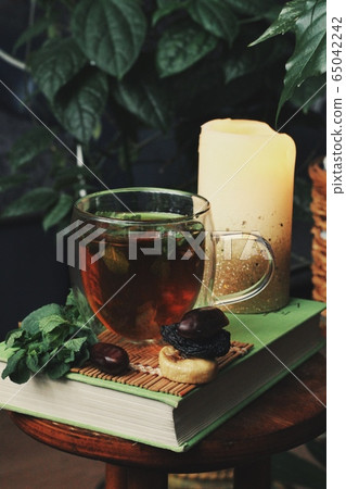 Dark mystic and calm mood. Book and hot tea with mint and honey on table with green plant Dark mystic and calm mood. Book and hot tea with mint and honey on table with green plant 65042242