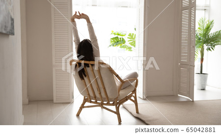 Back view of woman stretch relax in armchair at home 65042881