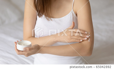 Young woman apply moisturizing body cream on arm 65042892