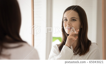 Young woman look in mirror do facial procedures 65043021