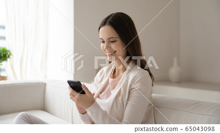 Caucasian girl sit on couch using cellphone gadget 65043098