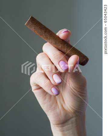 Cigar in woman hand, photo on gray background Cigar in woman hand, photo on gray background 65043423