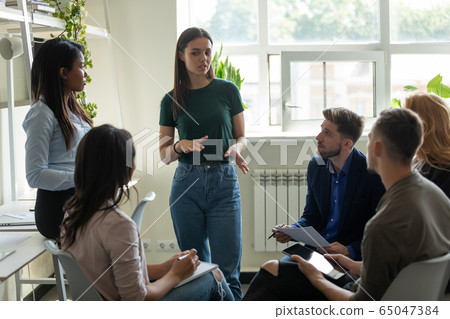 Serious female leader, mentor holding briefing for multiracial team interns. Serious female leader, mentor holding briefing for multiracial team interns. 65047384