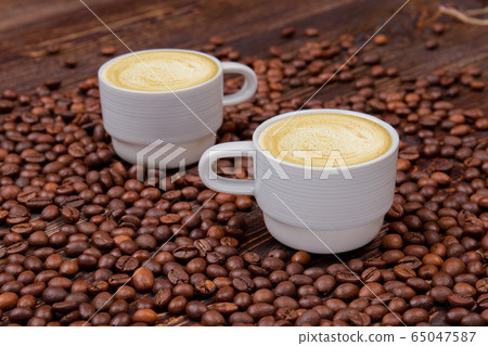 Two white cups of cappuccino on coffee beans heap. Two white cups of cappuccino on coffee beans heap. 65047587
