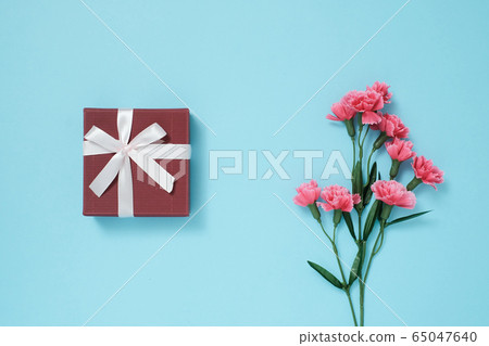 Present box with ribbon on light blue background and pink carnation Present box with ribbon on light blue background and pink carnation 65047640
