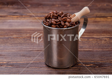 Short wooden scoop into steel mug with coffee beans. 65047691