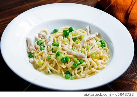 A white bowl filled with pasta and broccoli on a plate A white bowl filled with pasta and broccoli on a plate 65048728