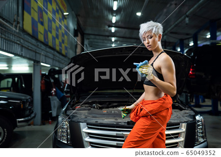 Girl mechanic checks engine oil. Scheduled oil change in the car. Car service. Girl mechanic checks engine oil. Scheduled oil change in the car. Car service. 65049352