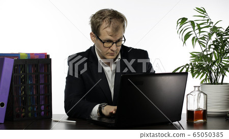 Tired disheveled businessman sitting at the table. Working hard in office Tired disheveled businessman sitting at the table. Working hard in office 65050385
