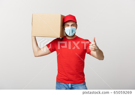 Cheerful young handsome delivery man holding a cardboard box and showing his thumb up while standing against grey background Cheerful young handsome delivery man holding a cardboard box and showing his thumb up while standing against grey background 65059269