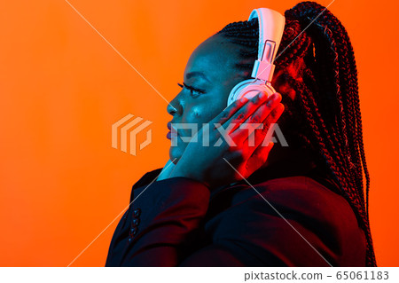 Young african-american woman listening to music in headphones in neon light. Female portrait. Concept of human emotions, facial expression, holidays or weekend, hobby, 65061183