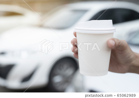 Woman hold paper cup coffee of hot in hand while standing car on the side before driving a vehicle in the morning sunlight. transportation and vehicle concept. Woman hold paper cup coffee of hot in hand while standing car on the side before driving a vehicle in the morning sunlight. transportation and vehicle concept. 65062989