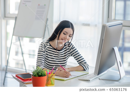 Dark-haired pretty woman in a striped shirt making notes Dark-haired pretty woman in a striped shirt making notes 65063176