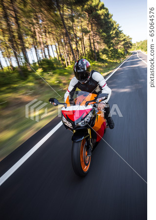 Orange color motorcycle with a driver in helmet 65064576